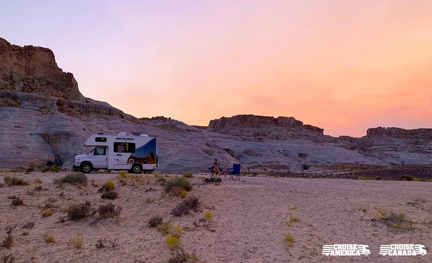 RV with a desert mountain backdrop and a man sitting in a camping chair