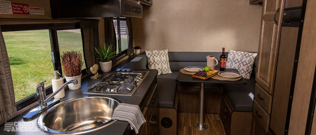 The kitchen and dining area of a Cruise America Compact Plus RV.